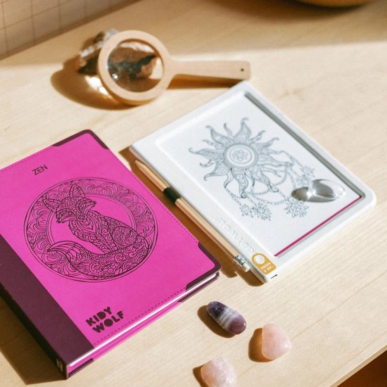 Roze Kidywolf Zen-tekenblok met vossenmotief naast een wit digitaal tekenbord, vergrootglas en edelstenen op tafel.