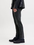 Zijaanzicht van een model in een grijze slim fit jeans en zwarte leren jas.