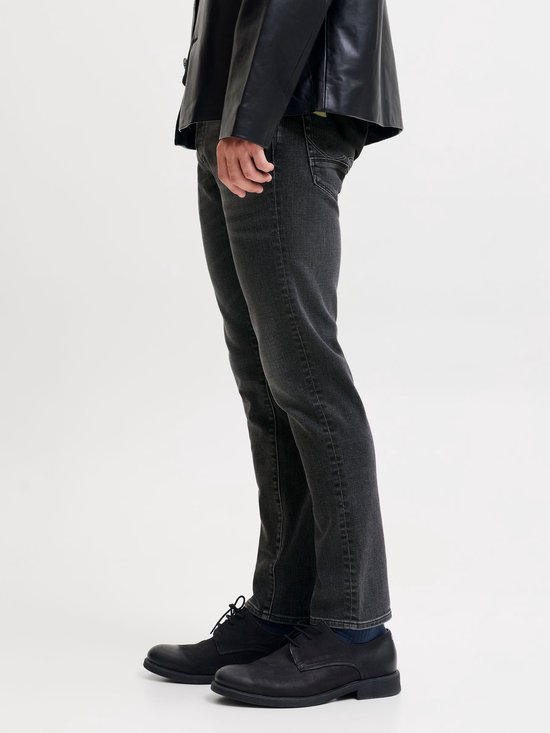 Zijaanzicht van een model in een grijze slim fit jeans en zwarte leren jas.