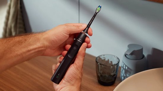 Zwarte elektrische tandenborstel van Philips Sonicare in handen, met opzetborstel en reisetui.