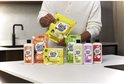 Persoon houdt een assortiment Marcel's Green Soap afwasproducten en navulverpakkingen vast op een keukenwerkblad.