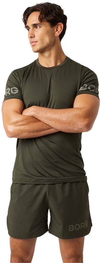Man in een donkergroen sportshirt met logo op de mouwen en bijpassende donkergroene sportshort.
