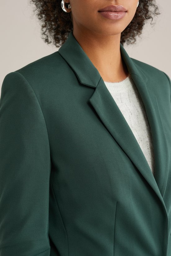 Donkergroene blazer met een lichtgroene trui eronder, gedragen door een model.
