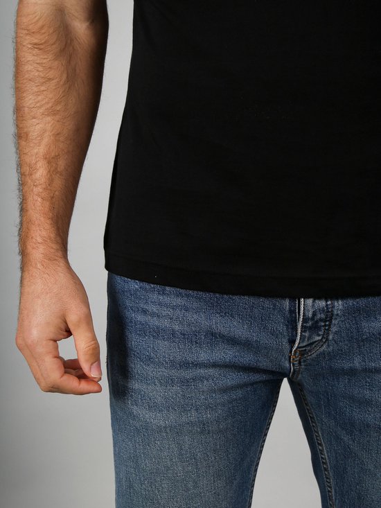 Gedetailleerde opname van de onderkant van een zwart T-shirt en een deel van een blauwe jeans, met de hand van een man.