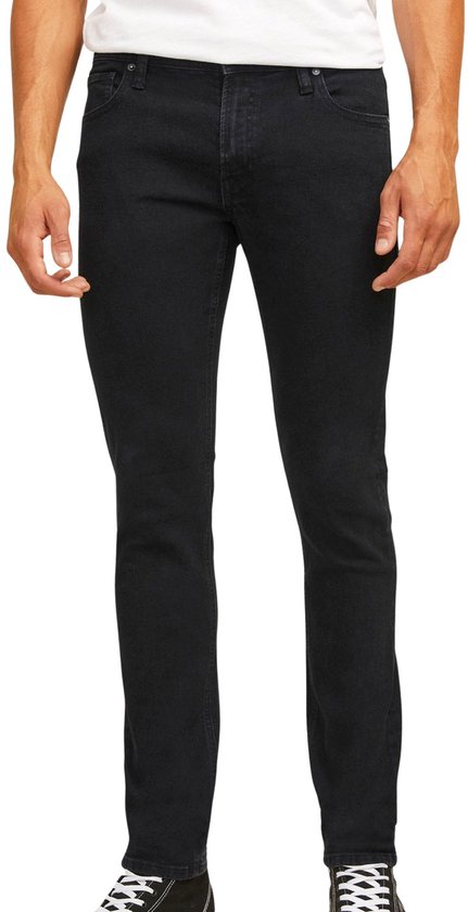Man in een strakke zwarte jeans en zwarte sneakers, vooraanzicht.
