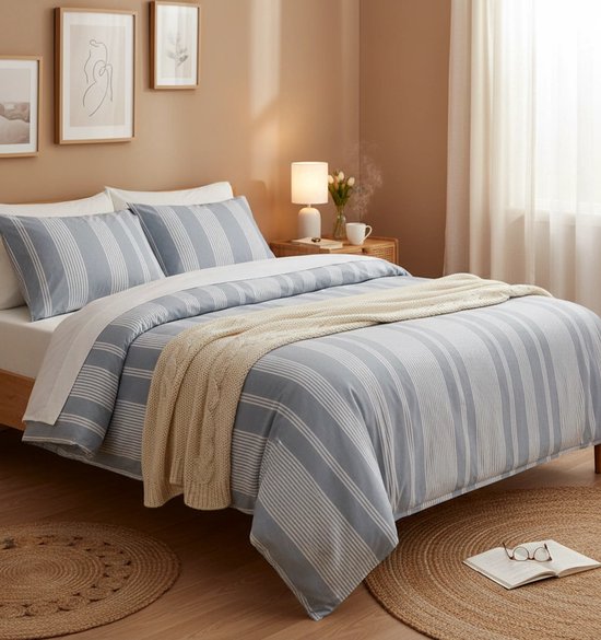 Blauw gestreept dekbedovertrek met beige gebreide plaid op een bed met houten hoofdeinde, twee ronde vloerkleden.