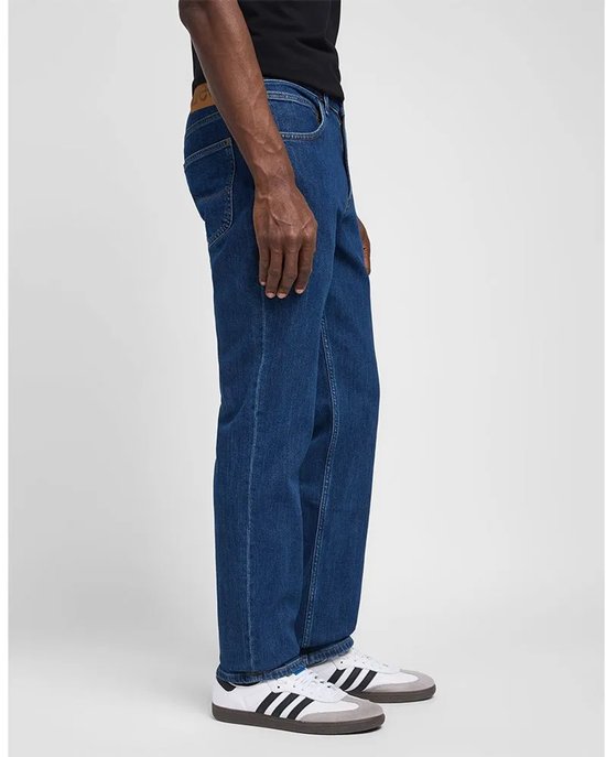 Man in donkerblauwe Lee jeans met rechte pasvorm, gedetailleerde naden en een bruin merklabel.