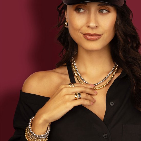 Vrouw met gouden en zilverkleurige kettingen met balletjes en bijpassende armbanden en ringen.