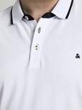Close-up van de kraag en knoopsluiting van een witte poloshirt met zwarte biezen en een klein logo.