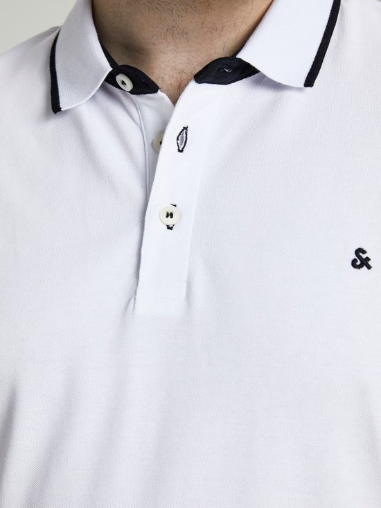 Close-up van de kraag en knoopsluiting van een witte poloshirt met zwarte biezen en een klein logo.