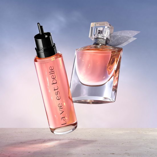 La Vie est Belle parfumflacon en navulfles met roze vloeistof zweven tegen een achtergrond van lucht.