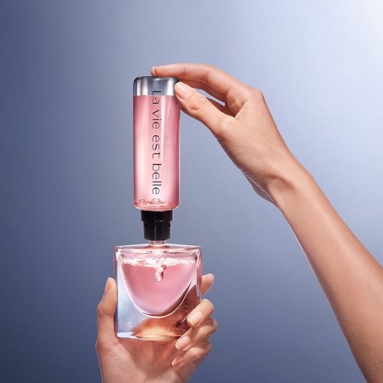Handen vullen Lancôme La Vie est Belle parfumfles bij met een navulfles. Roze parfum.