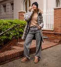 Vrouw met grijze jeans, beige trui, grijze lange jas met bontkraag en bruine UGG-sneakers.