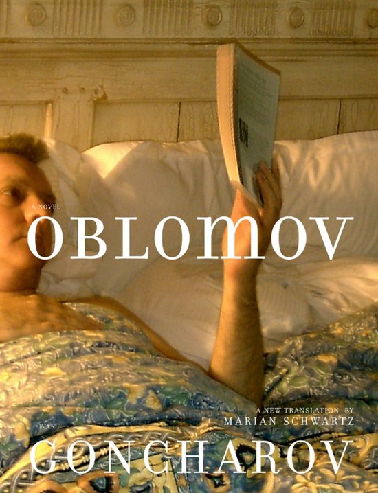 Een man ligt in bed, bedekt met een deken met een groen en blauw bloemenpatroon, en leest een boek met de titel "Oblomov".