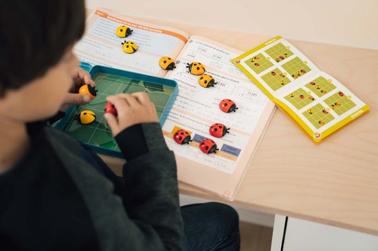 Un garçon joue à LogiBugs, avec le plateau de jeu ouvert et le livret de règles.