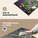 Zwarte inductiebeschermer met betonprint, bedekt met kruiden, knoflook, citroen en peperkorrels, afgeveegd met een doek.