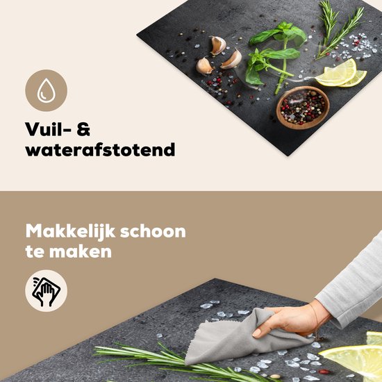 Zwarte inductiebeschermer met betonprint, bedekt met kruiden, knoflook, citroen en peperkorrels, afgeveegd met een doek.