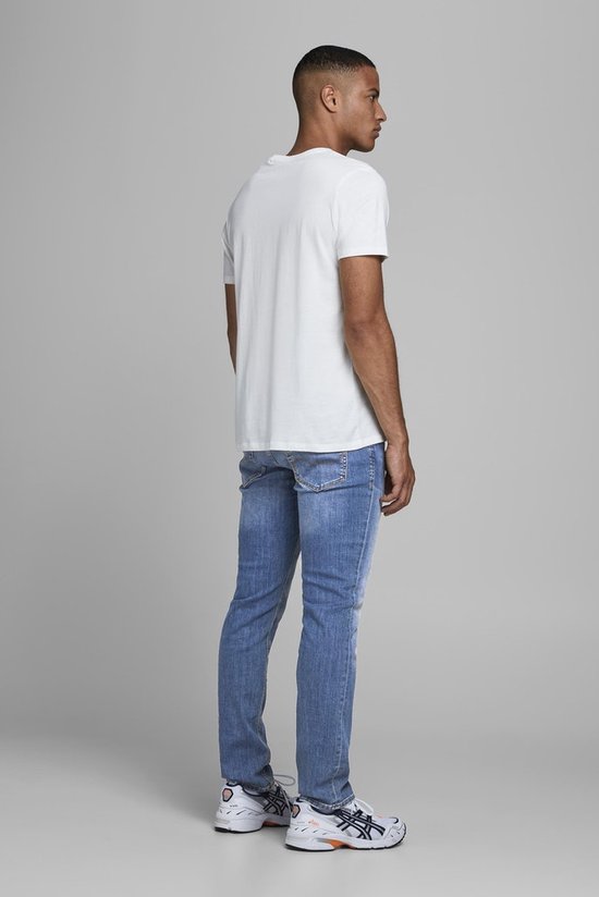 Man draagt een wit T-shirt en een lichtblauwe spijkerbroek met lichte schade.