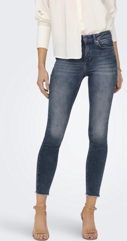 Model in witte blouse en donkerblauwe skinny jeans met rafelige zoom.