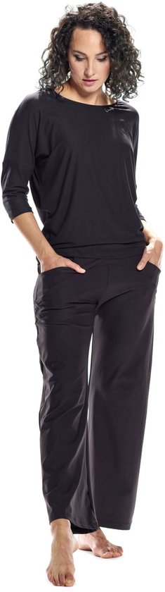 Model draagt een zwarte, wijde driekwartmouw top en zwarte broek met hoge taille en steekzakken. Handen in de zakken.