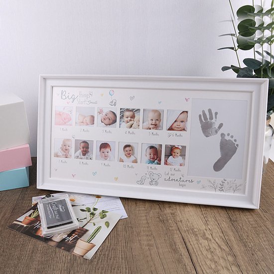 Cadre photo blanc avec 12 photos de bébés de 1 à 12 mois, avec espace pour empreintes de main et de pied. Texte 'Big things Start Small' et 'Let our adventures begin'. Sur fond de bois, à côté d'objets décoratifs.