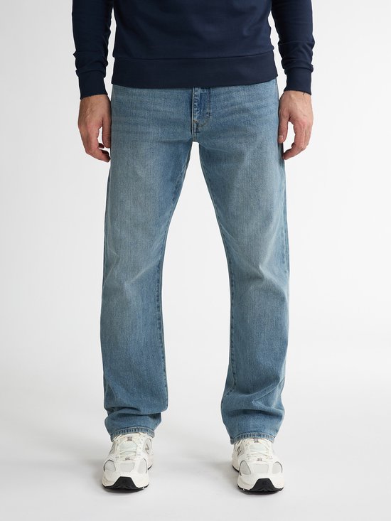 Man draagt een blauwe jeans en een donkerblauwe trui, staand.
