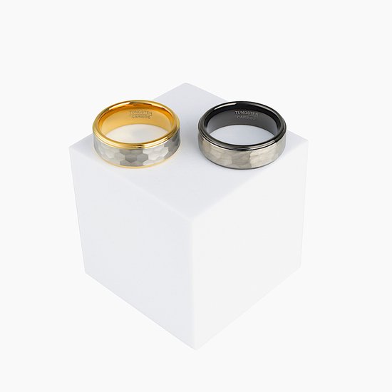 Gouden ring met grijs gehamerd stalen middenstuk en grijze ring met gehamerd middenstuk op witte kubussen.
