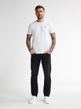 Man met tattoos op de armen in een wit T-shirt en zwarte jeans.