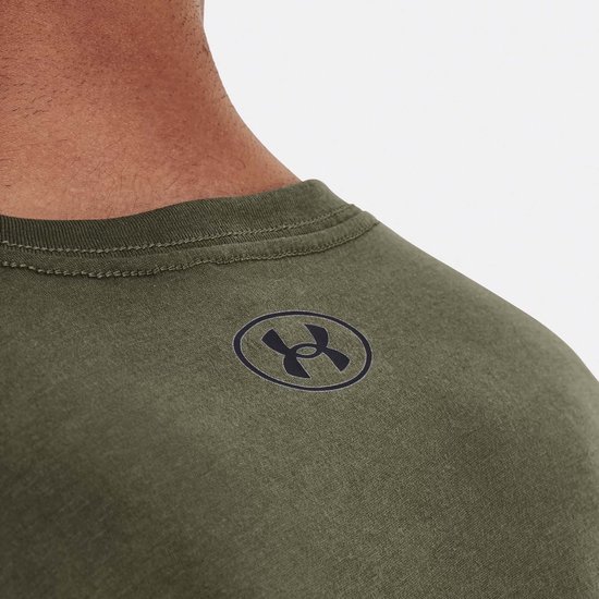 Close-up van de nek en schouder van een man in een legergroen T-shirt met korte mouwen. Een cirkelvormig logo met een Under Armour-logo is zichtbaar.