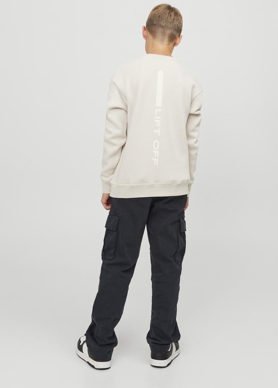 Jongen in crème sweater met 'Lift Off' op de rug en een donkerblauwe cargobroek.