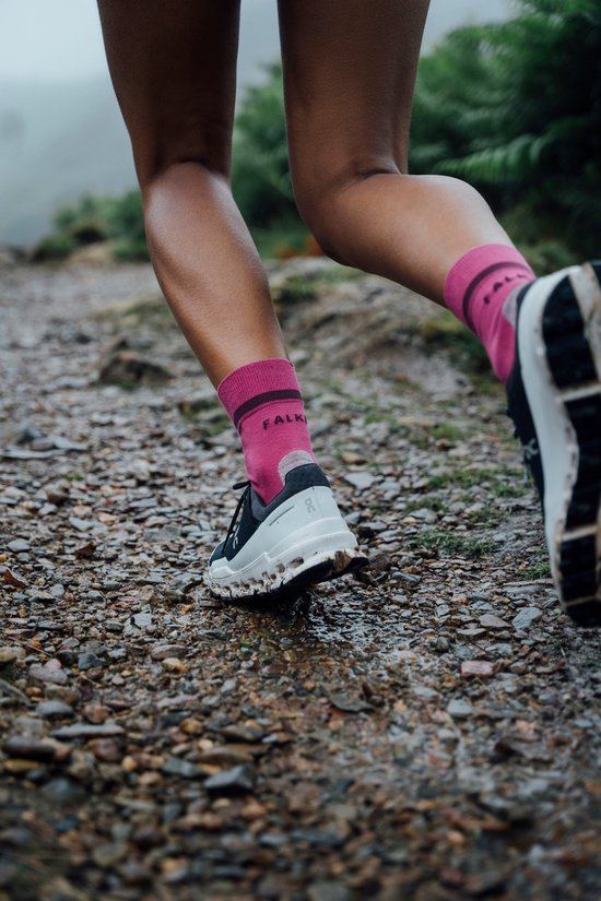 Voeten van een vrouw die rent op een modderig pad, draagt roze Falke sokken en zwarte schoenen.