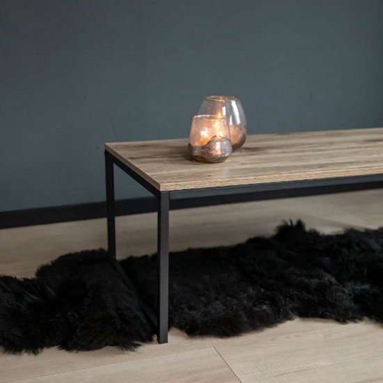 Salontafel met licht houten blad en zwart stalen frame. Twee glazen windlichten met kaarsen erop.
