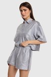 Model draagt een zilverkleurig, glanzend cropped overhemd met korte mouwen en bijpassende shorts.