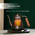 Zwarte waterkoker met houten handvat, water kookt op een verwarmingsplaat. Blijft tot 2 uur warm.