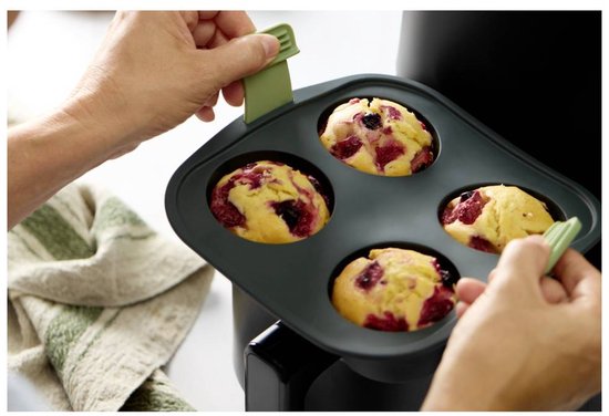 Grijze siliconen bakvorm met 4 ronde uitsparingen, gevuld met vier bessenmuffins, verwijderd uit een zwarte heteluchtfriteuse.