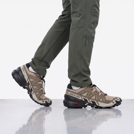 Voeten in beige Salomon Speedcross 6 trailrunningschoenen met groene broek, in beweging.