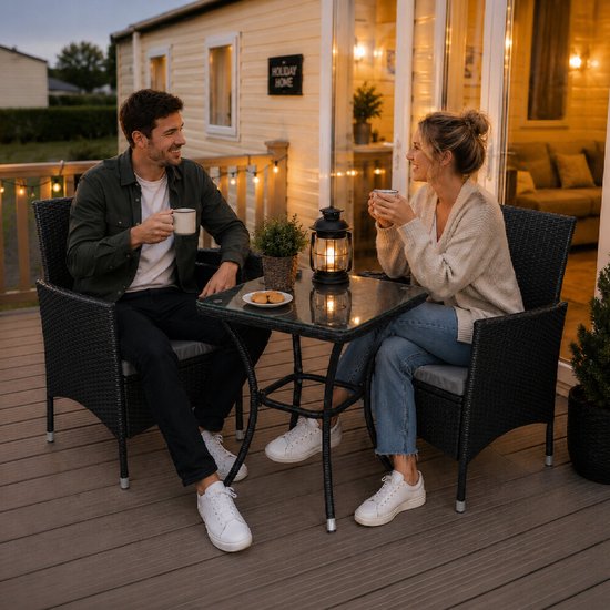 Koppel op een houten dek bij een caravan, genietend van koffie aan een zwarte rotan bistroset.