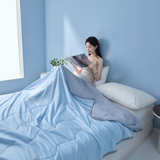 Vrouw leest een boek onder een lichtblauwe en grijze deken.