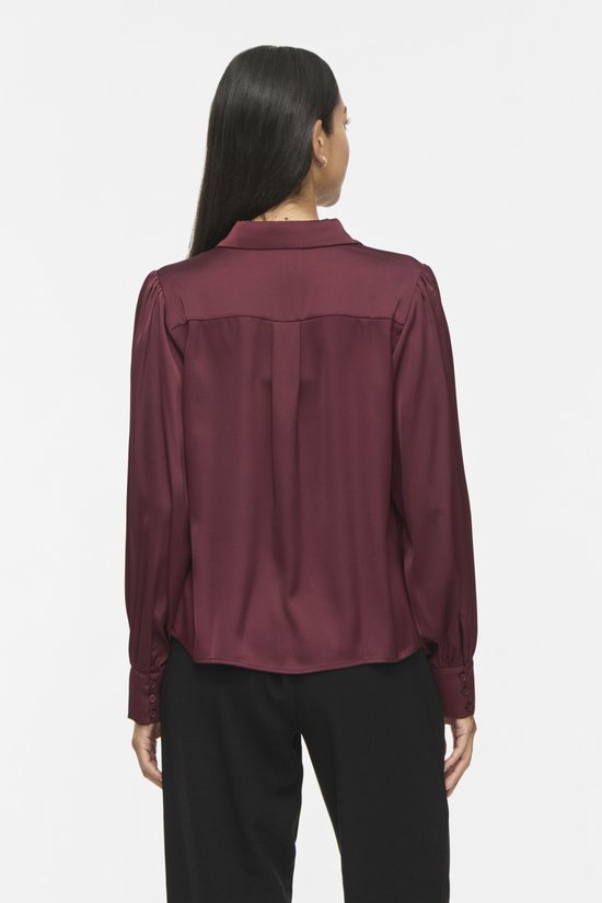 Achterkant van model in bordeauxrode satijnen blouse met lange pofmouwen en zwarte broek.