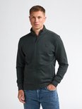 Man met donkergroen vest met rits, hoge kraag en jeans.