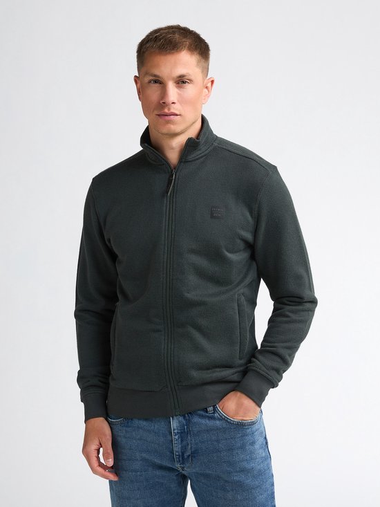 Man met donkergroen vest met rits, hoge kraag en jeans.