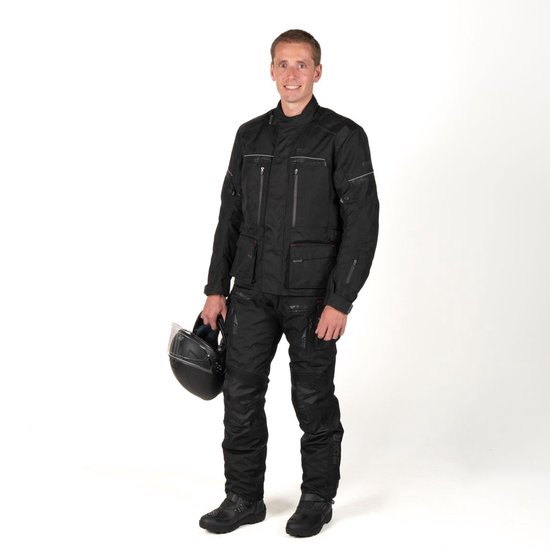 Man in een zwarte motorjas en -broek van DXR, met helm in de hand.