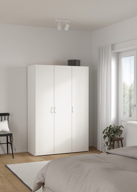 Witte driedeurskast in een slaapkamer, met naast het bed en een raam.
