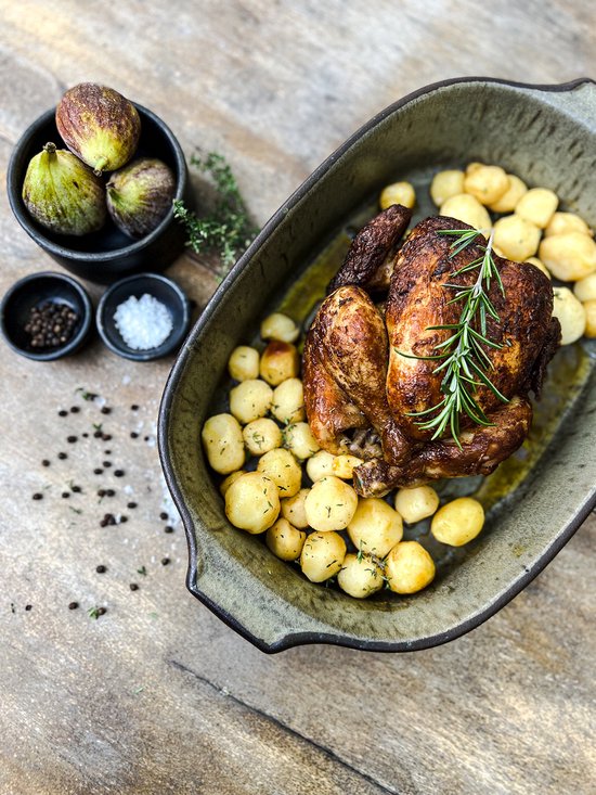 Gegrilde kip met aardappelen, vijgen en kruiden in een groene ovenschaal.