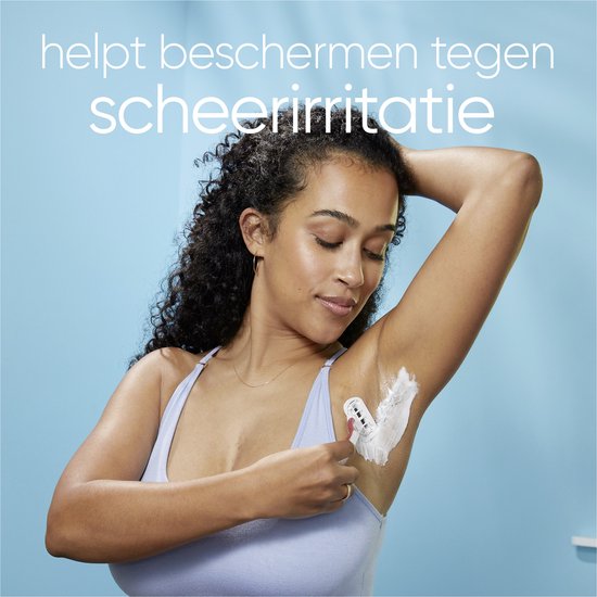 Vrouw met krullend haar scheert haar oksel in een badkamer. Tekst: 'helpt beschermen tegen scheerirritatie'.