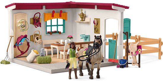 Een meisje en een bruin paard met groen halster staan in een stal. Een zadel en een kat zijn ook aanwezig.