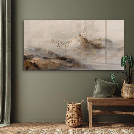 Een acrylglas schilderij met een berglandschap in mistige, beige en bruine tinten. Een zwerm vogels vliegt voor de besneeuwde bergtoppen.