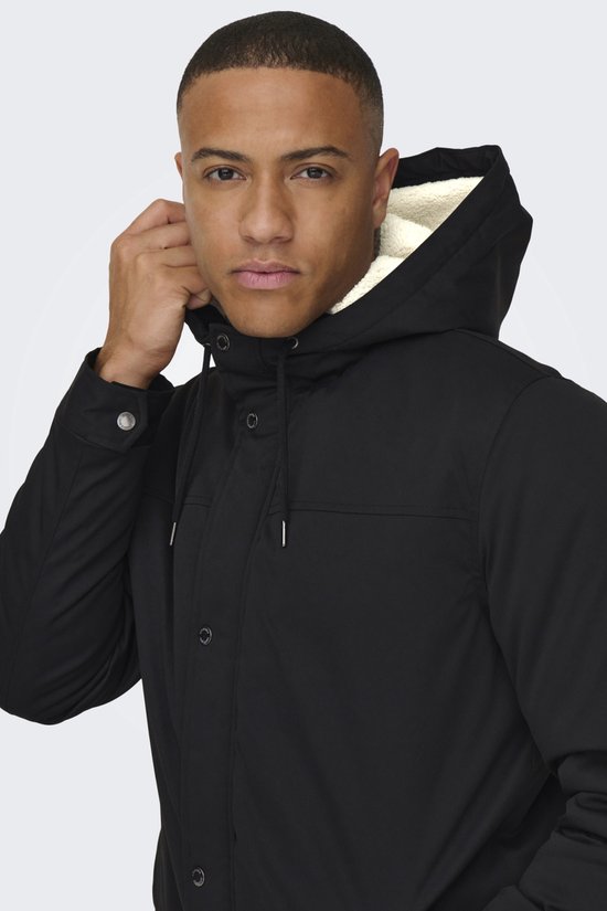 Close-up van man die capuchon van zwarte parka met witte imitatiebontvoering vasthoudt.