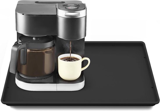 Zwarte mat onder een koffiezetapparaat dat koffie zet in een gele mok.