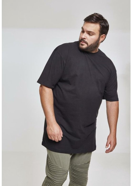 Een man met een baard draagt een zwarte oversized T-shirt en olijfgroene broek.